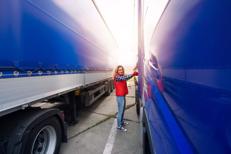 Female trucker removing canvas tarpaulin to prepare truck for unloading.