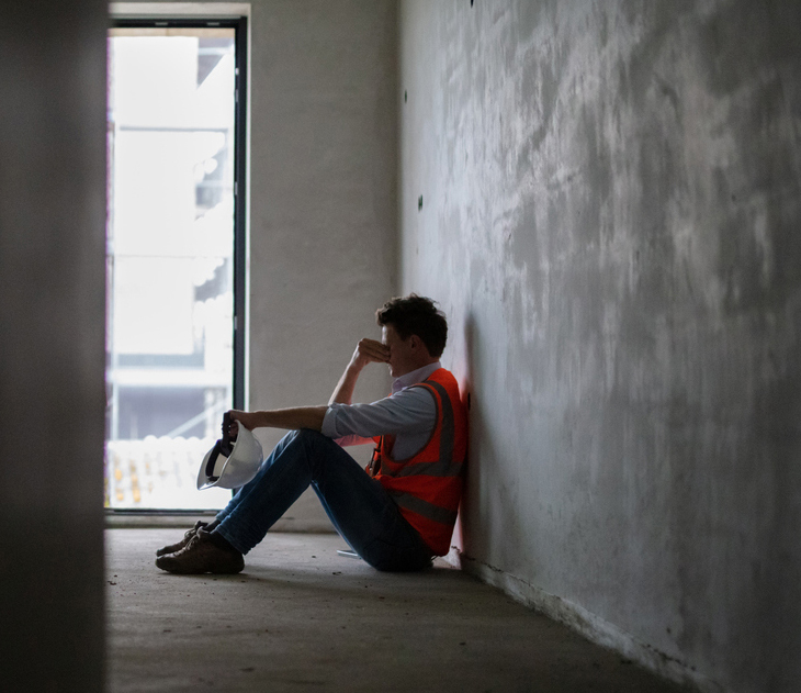 Depressed building contractor sitting inside incomplete house at construction site