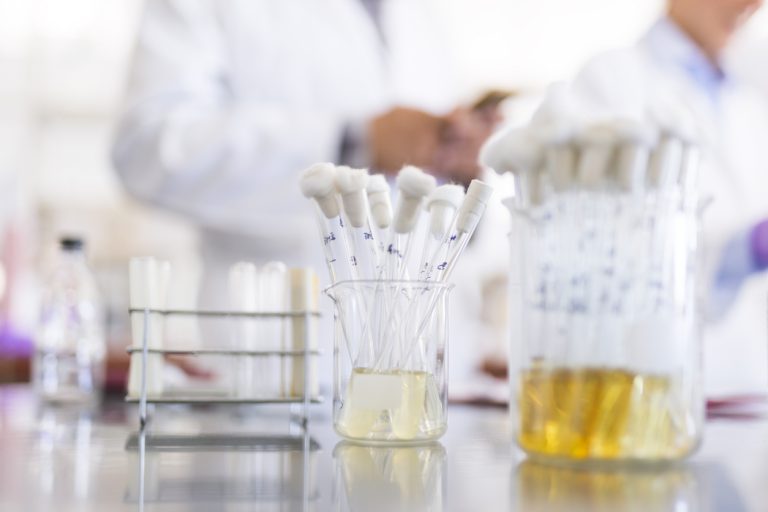 Test tubes with chemical samples in a jar, scientist working in the background